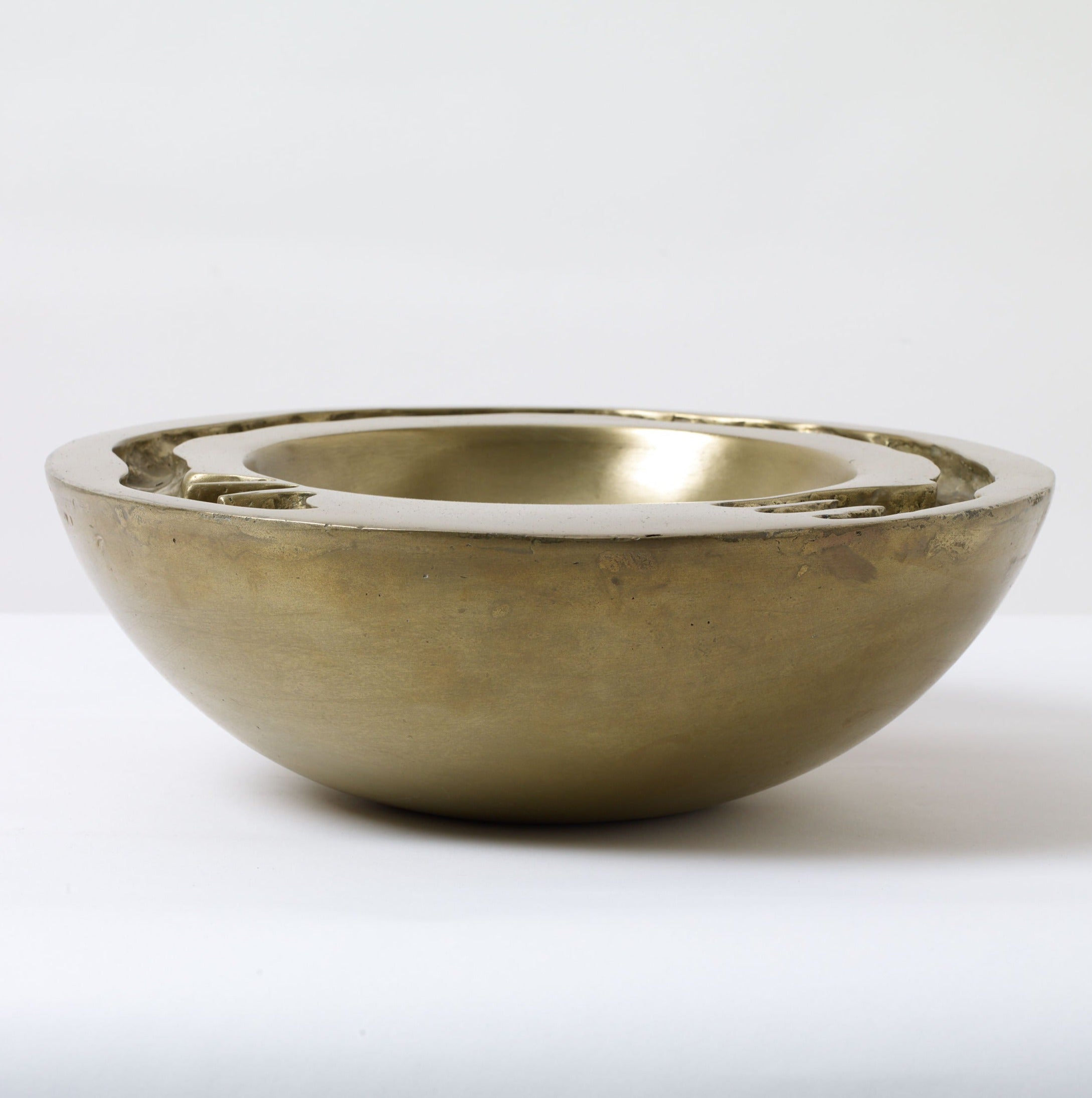 A simple, large Signature Dish Brass Sculpture from Lucy Page with a tarnished exterior and a shiny interior, placed against a plain white background.