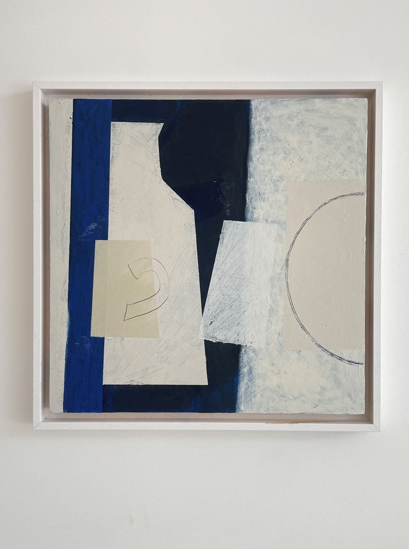 A framed Blue Still Life I abstract acrylic painting on a wall, featuring geometric shapes in shades of blue, white, and a touch of beige by Lara Voce.