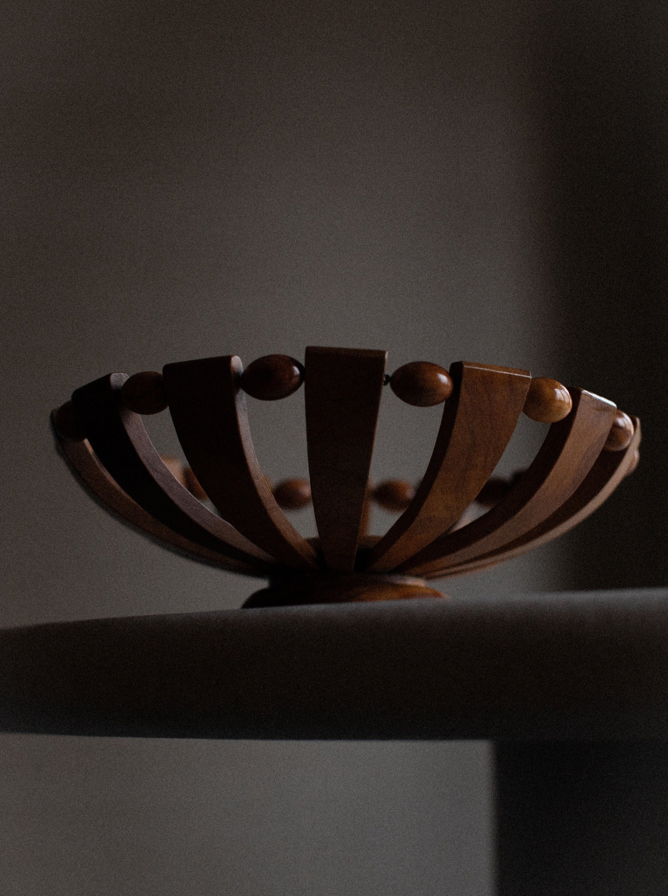 A Out For Lunch 1950's Art Deco bowl with a unique open design featuring vertical slats topped with small round knobs, showcasing the natural grain, situated on a grey surface against a dimly lit background.