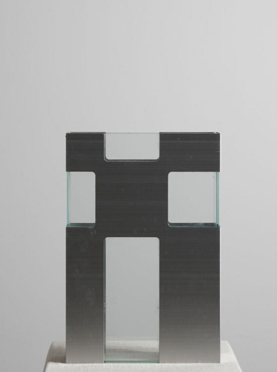 A minimalist sculpture of a Block Vase made from dark-colored material and clear plexiglass components, depicted against a plain gray background by Les Objets Amsterdam.