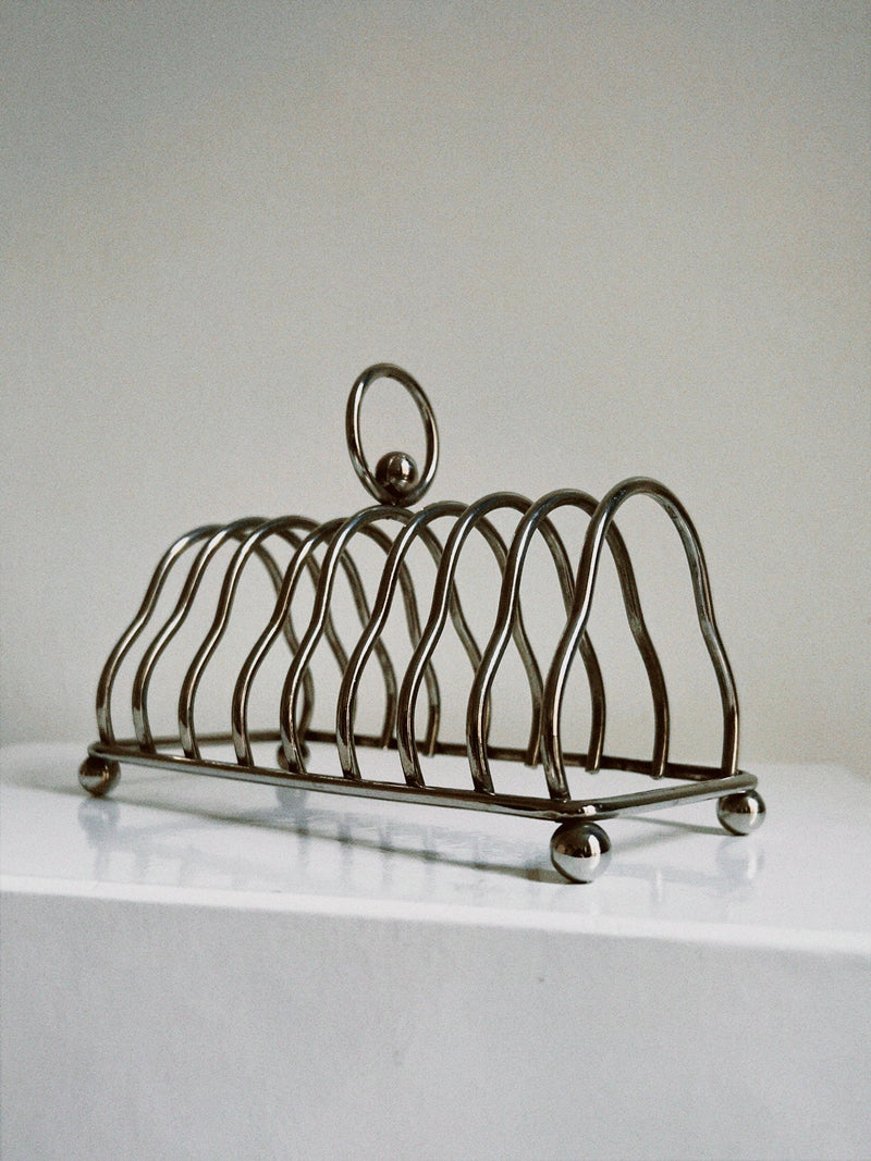 An elegant Manushi Art Deco Toast Rack with curved holders and a sleek design, standing on a white surface against a neutral background.