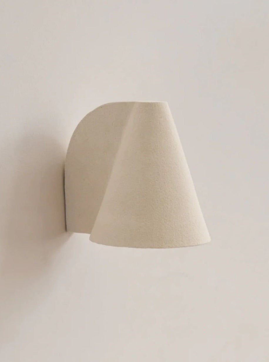 An abstract, beige ceramic sculpture with a soft, curved shape attached to a Mariza Galani Esoteric Wall Lamp, casting a subtle shadow.