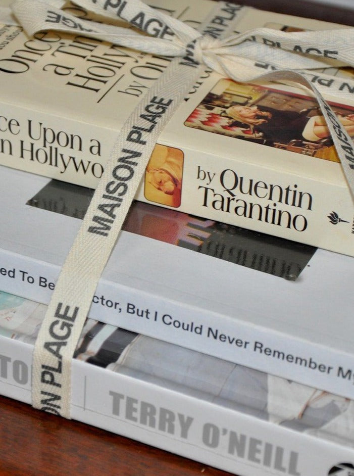 A stack of Maison Plage's "The Hollywoodland Stack" books tied with a cream ribbon on a wooden table, focusing on detailed book covers and elegant packaging.