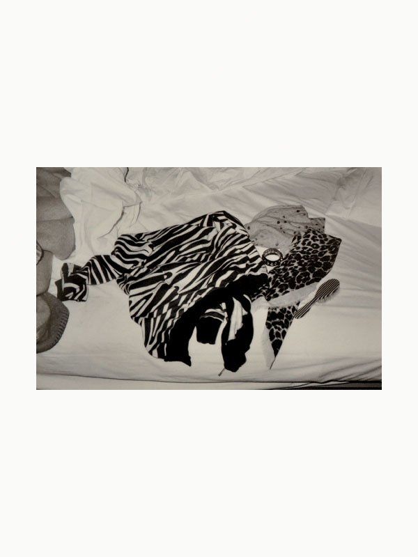 A conceptual art collection of clothes with animal prints, including zebra and leopard patterns, laid out on a crumpled white bedsheet from Maison Plage's Sophie Calle: The Hotel collection.