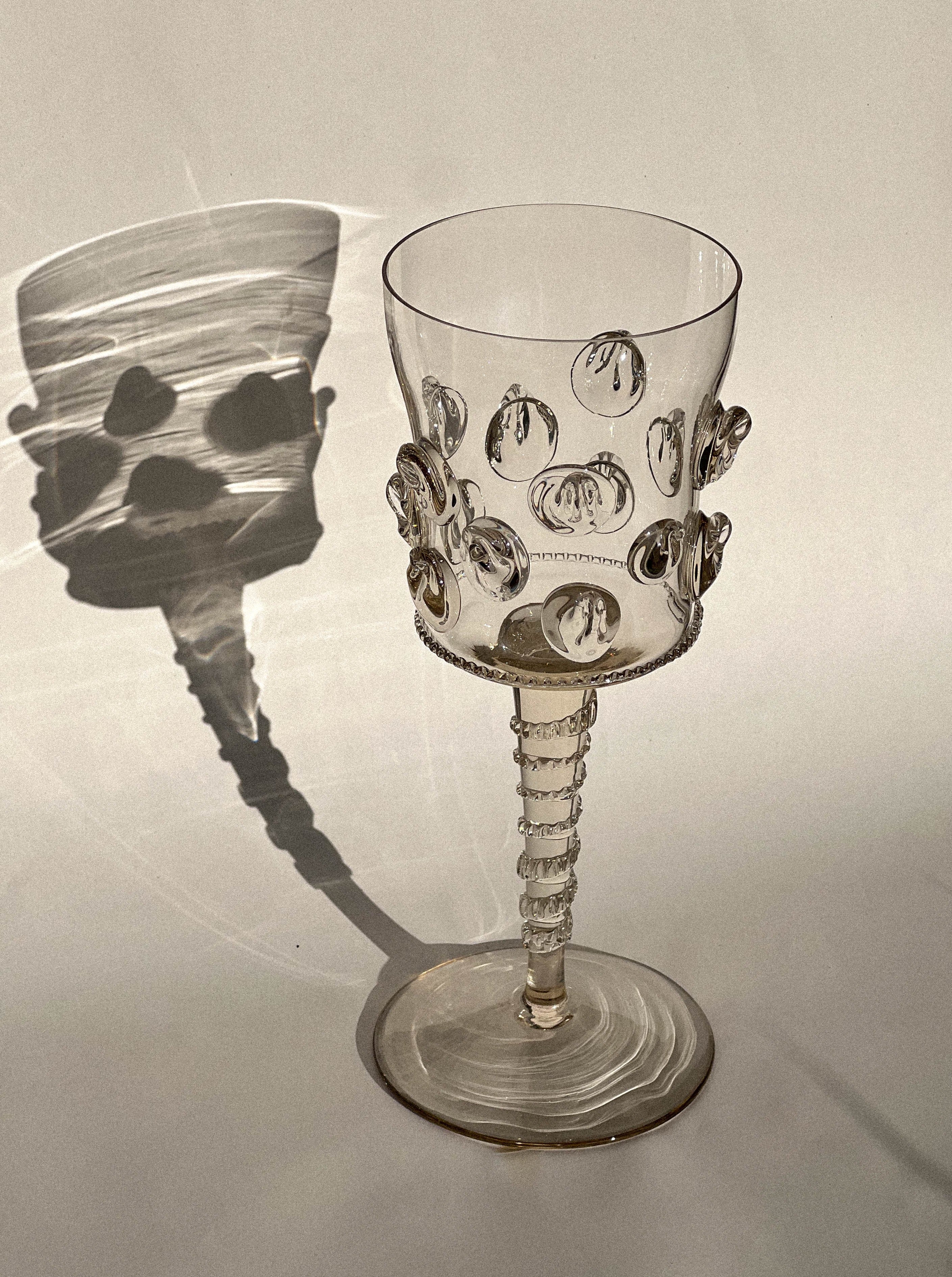 A Pair of Mouthblown Wine Glass - Dots by Lucie Claudia Podrabska with a shadow on the surface, showcasing the elegance of timeless artisanal techniques.