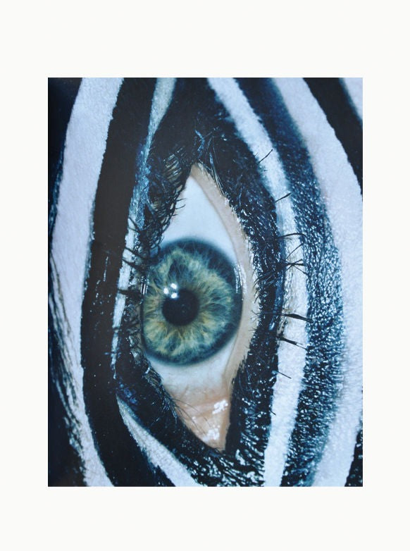 Close-up of a human eye with artistic black and white striped makeup, highlighting the textures and details of the iris and surrounding skin for Carlijn Jacobs - Eyes by Maison Plage photography book.