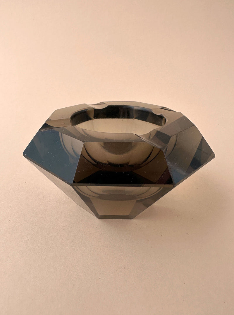 The Moser Crystal Glass Ashtray Prisma 30s from Dodo Vintage, characterized by its black, diamond-shaped design with a hollow center, is displayed against a beige background. Resembling an Art Deco ashtray, the piece features a shiny, polished surface and intricate geometric facets that reflect light beautifully.