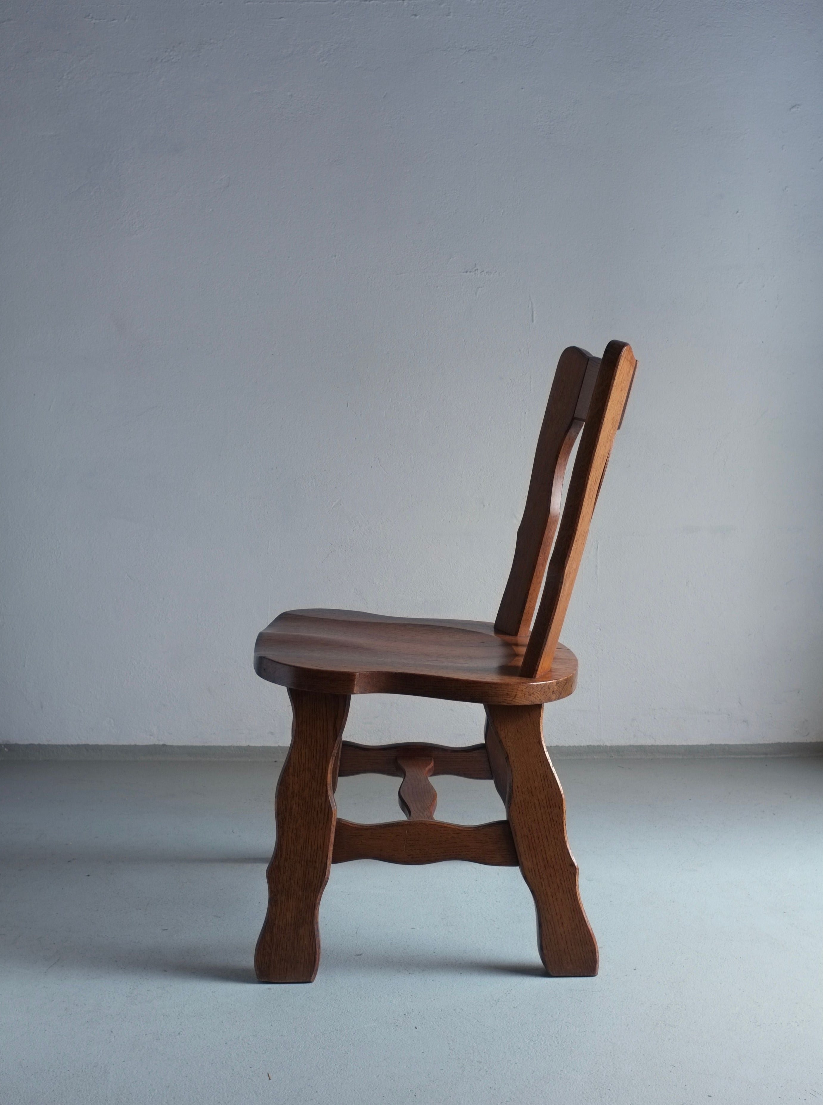 Two Veter Vintage Brutalist Carved Oak Dining Chairs from the 1970s stand against a plain, light gray background, casting a soft shadow on the floor. These chairs are in vintage condition.