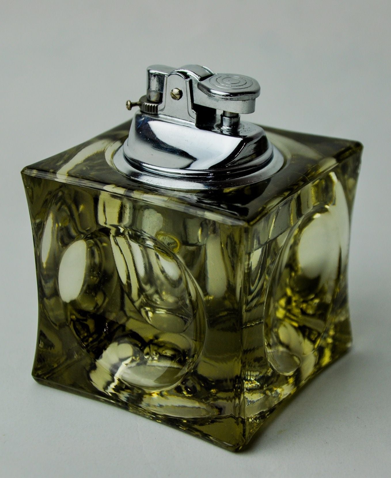 A square Murano glass ice cube lighter by Antonio Imperatore, 1970 containing yellow liquid, featuring a detailed metal spray nozzle and cap on a gradient gray background.