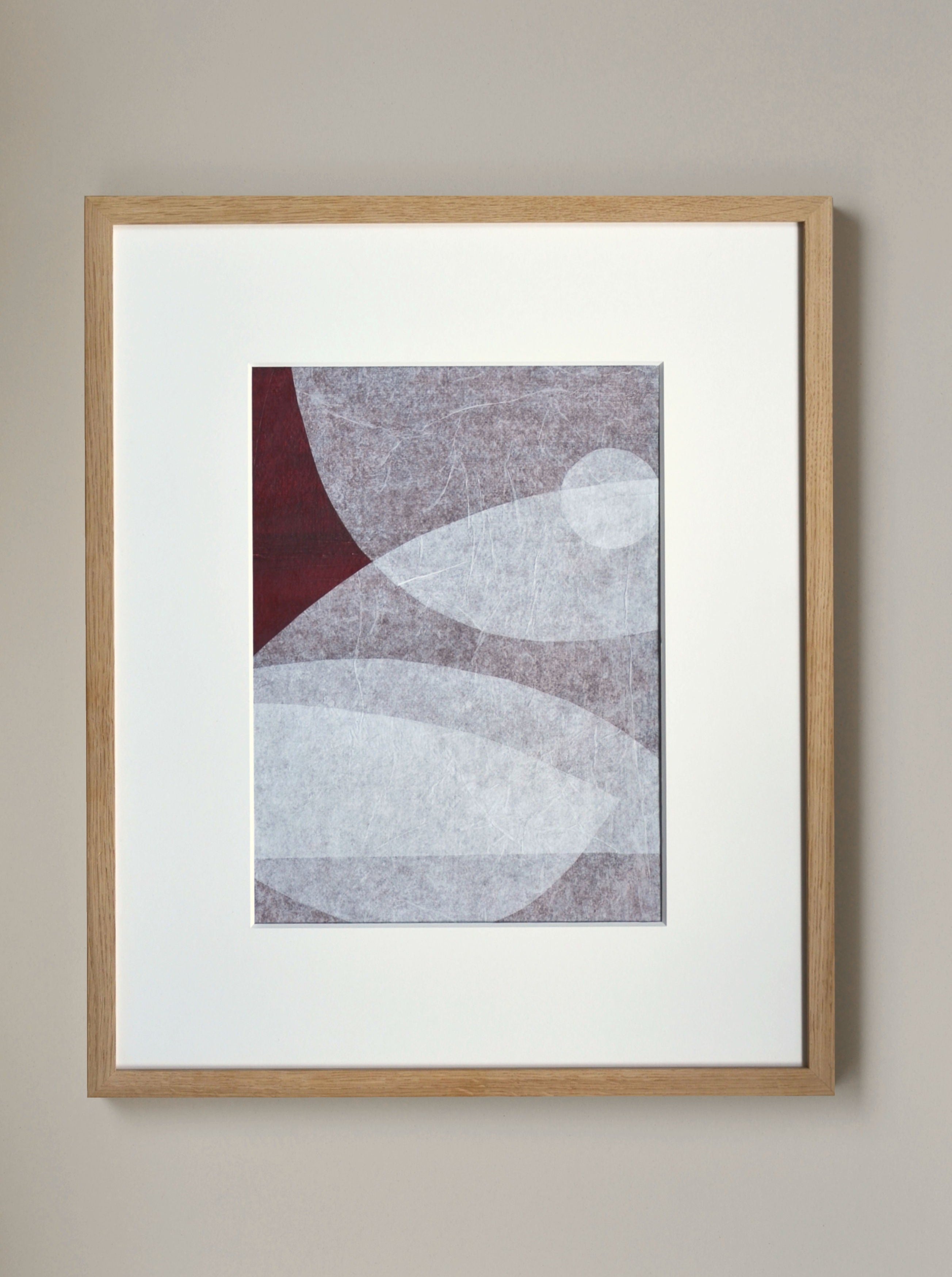 Abstract geometric artwork on handmade cotton paper in a wooden frame, featuring a composition of curved and angular shapes in shades of gray and burgundy on a white background by Julita Elbe's Moment.