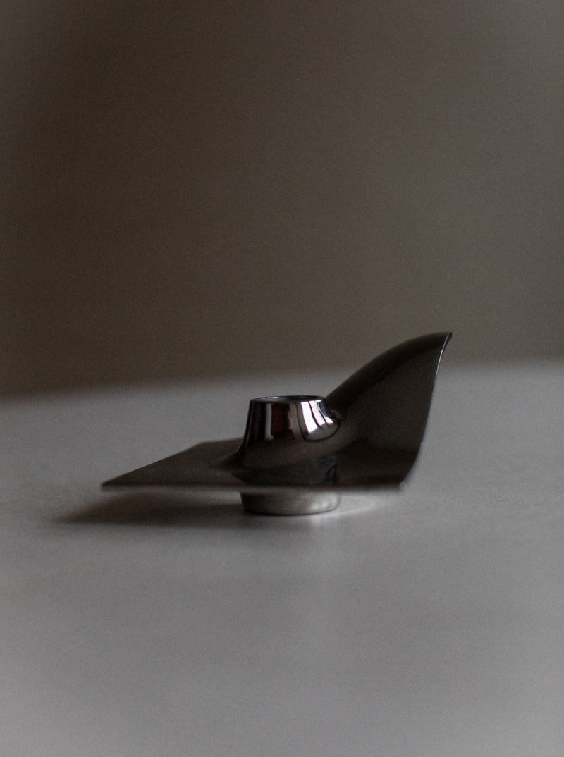 A 70's Chrome Candle holder by Out For Lunch set against a soft gray background, reflecting light on its organic structures and sleek, curved surface.