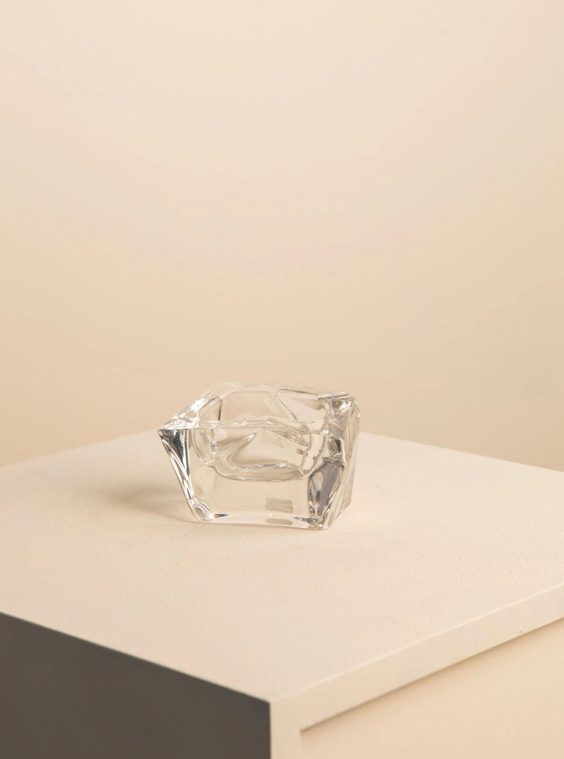 A small, delicate Free-Form Crystal Ashtray by Daum from the 60's, offered by Treaptyque, is placed on a light beige surface. The background features a gradient of soft, warm tones that evoke the classic elegance of vintage crystal designs.