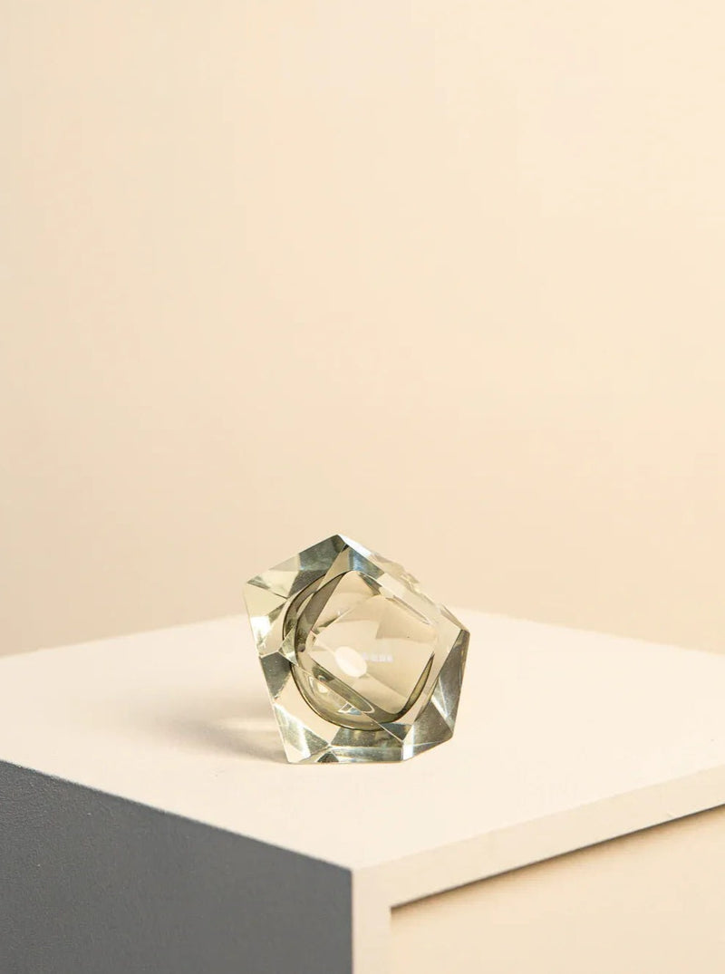 A Black "Diamant" ashtray in Murano glass by Flavio Poli for Seguso 60's sits on a white platform against a soft beige background, reflecting light and casting subtle shadows.
