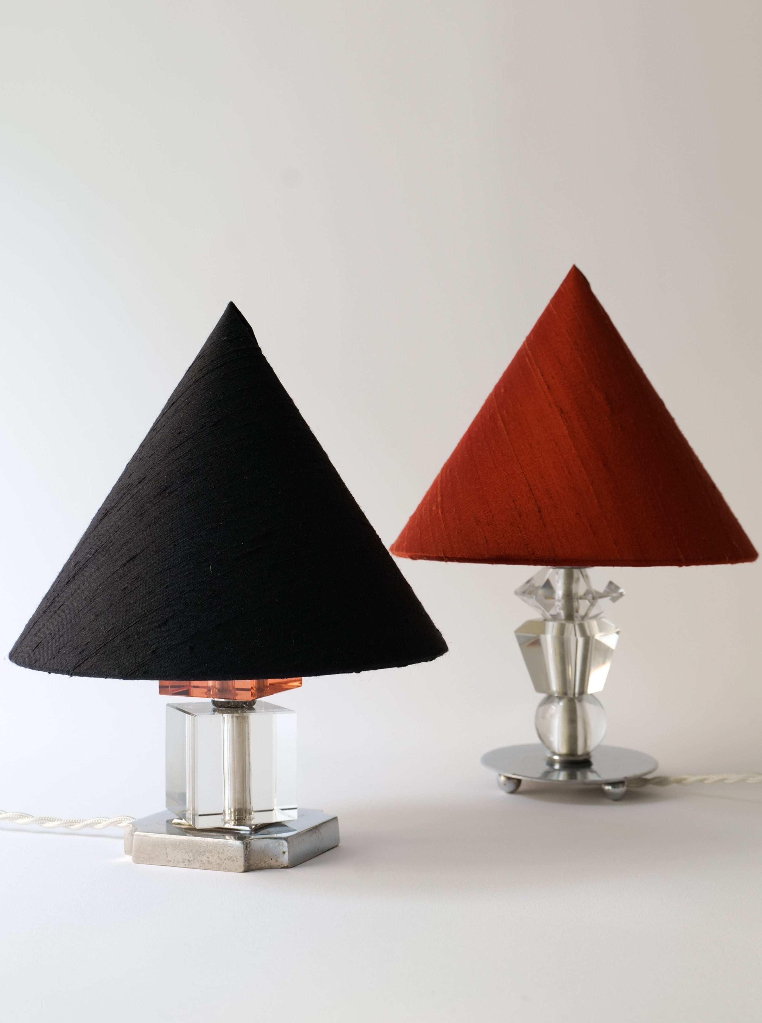 Two Deco Crystal table lamps from the Collection apart line with conical shades, one black and one red, displayed against a neutral background. Each lamp base features a modern metallic and glass design.