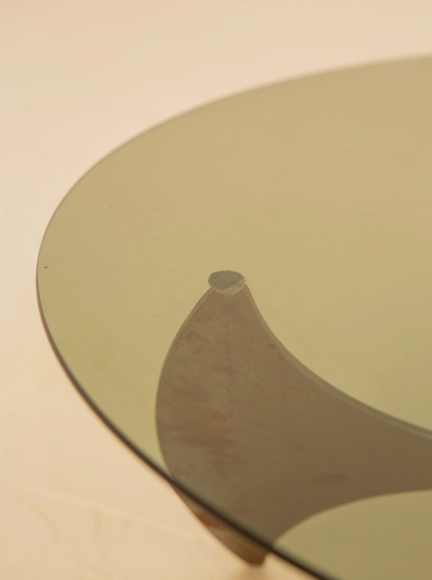 Close-up of the Propeller Circular Coffee Table by Knut Hesterberg for Treaptyque, featuring an artistic wooden base visible through the round glass top. Set against a neutral background, its minimalist design emphasizes the sleek form and smooth surface.