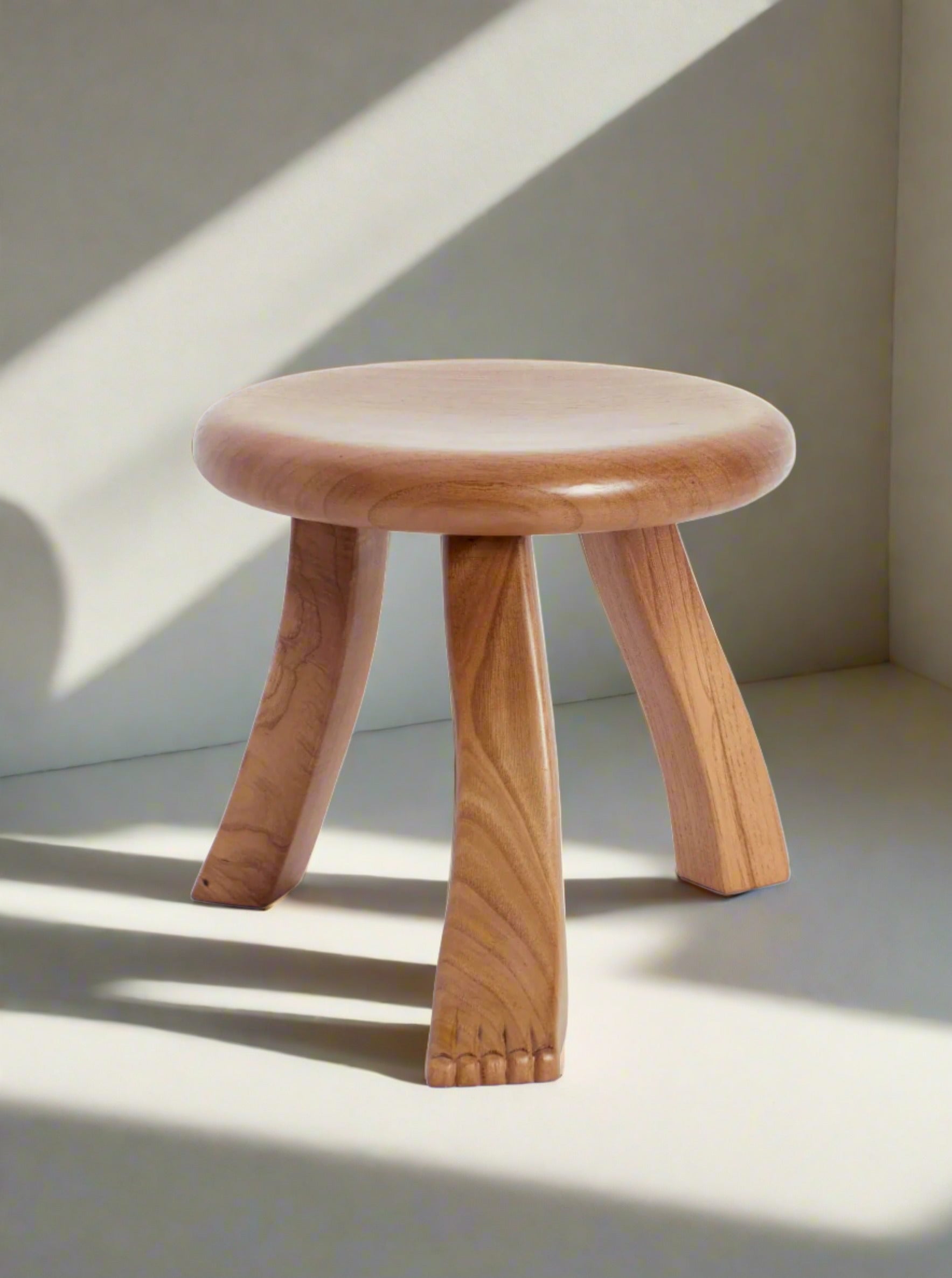 A handcrafted Project 213A foot stool in oak with a smooth, round seat and three splayed legs, set against a plain white background. The legs feature a subtle, organic curve, enhancing its simple yet elegant design.