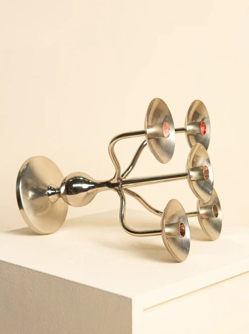 A sleek, modern metallic candle holder with five circular holders is displayed on its side against a minimalist, light-colored background. The Italian "Medusa" Silver-Plated Candleholder 70's by Treaptyque features a shiny, polished finish and a balanced, symmetrical structure reminiscent of 80s interior design.