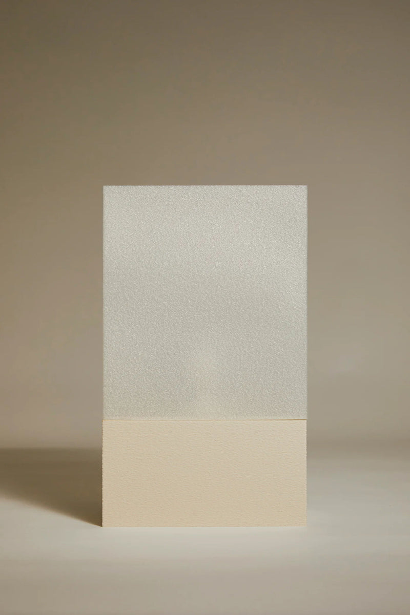 The Lampe i by Argot Studio features a vertical rectangular design with a sculptural flair: its textured, frosted upper half blends seamlessly into a smooth, beige lower half. Set against a soft, neutral background, it epitomizes elegance and contemporary style.