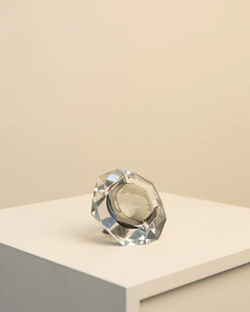 A large, multifaceted glass crystal designed by Flavio Poli for Seguso 60's, resting on a white pedestal against a beige background, reflecting light with its transparent and shiny surface.