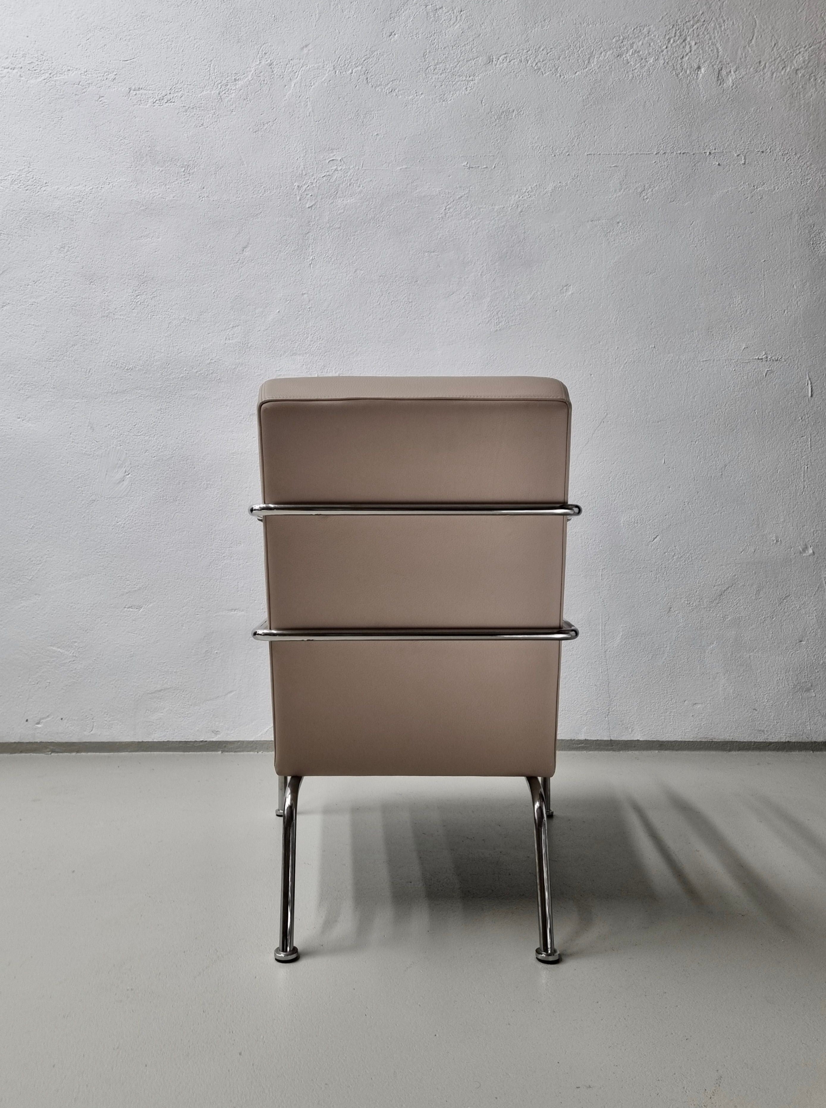 A beige modern-style chair by Gunilla Allard for Lammhults 1990s, positioned against a grey concrete wall, viewed from the front in a minimalist setting.