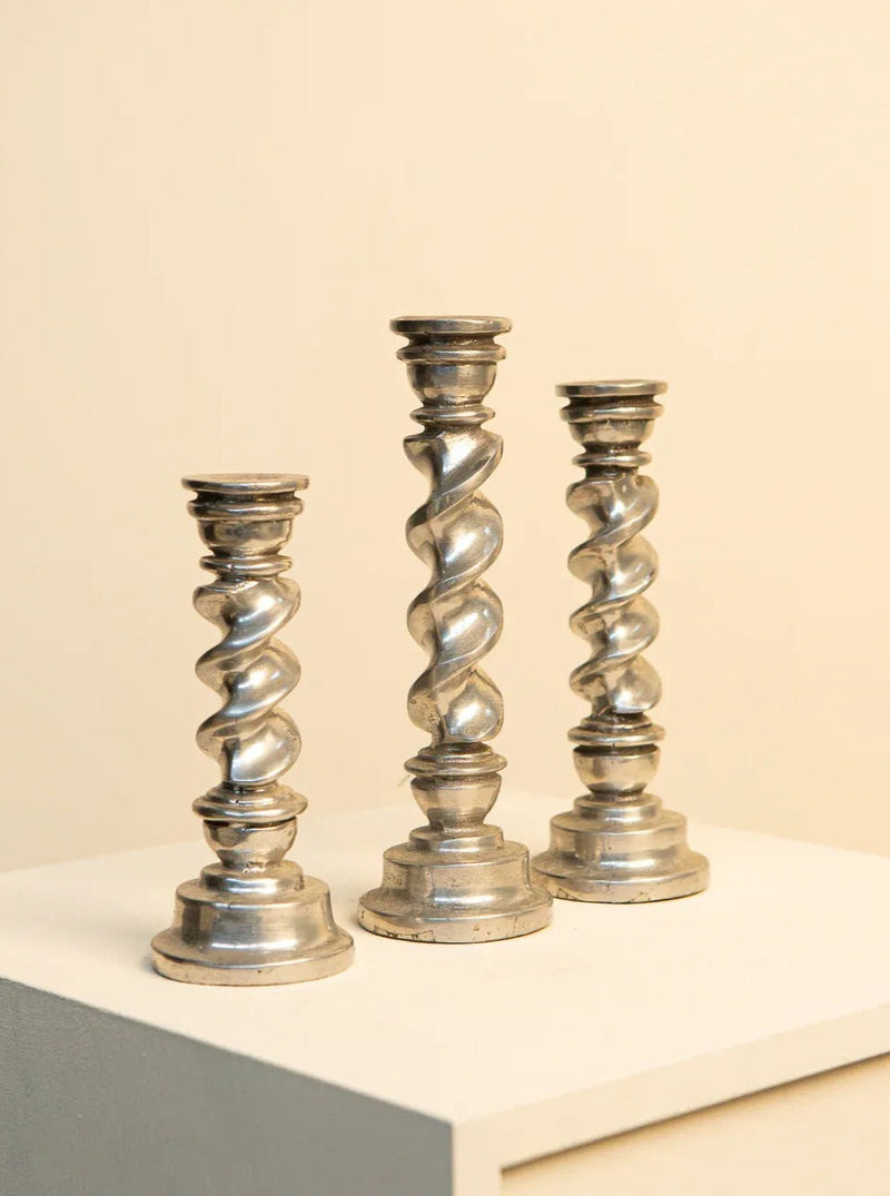 Three modern and artistic twisted aluminum candleholders in a triptych arrangement