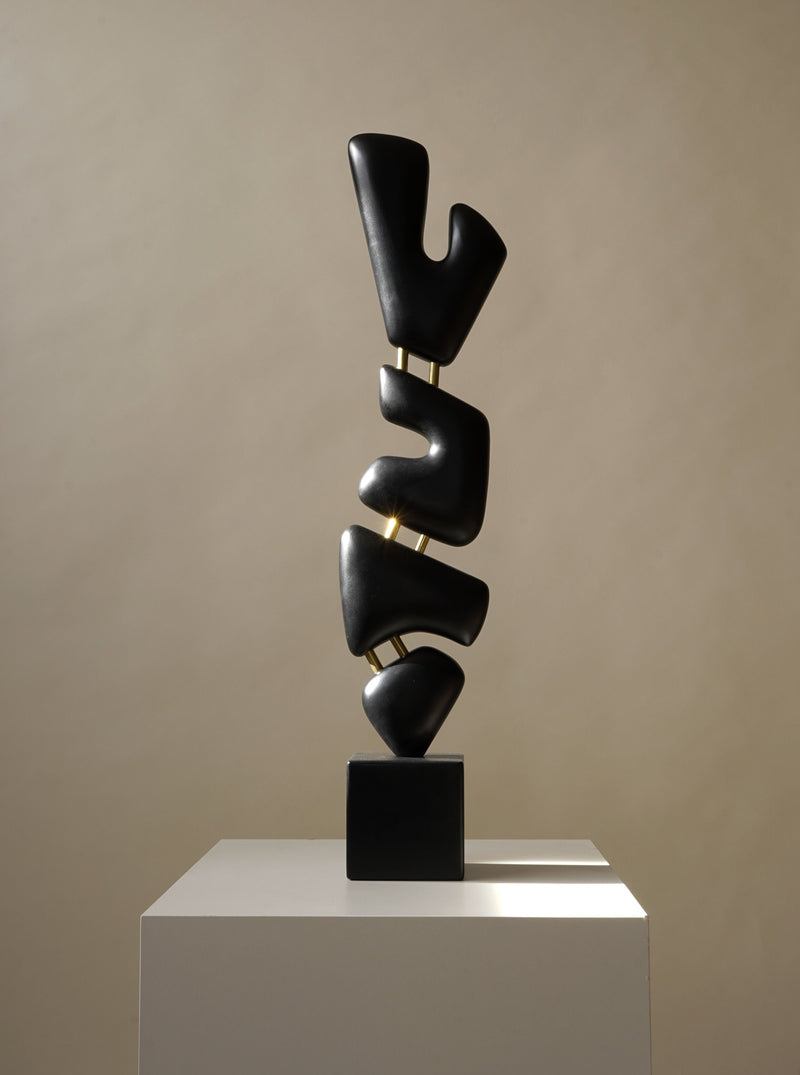 The Urbmon 116 Sculpture by Chandler McLellan is a modern, minimalist piece with handcrafted, smooth abstract dark forms stacked vertically on a pedestal, casting subtle shadows on a neutral backdrop.