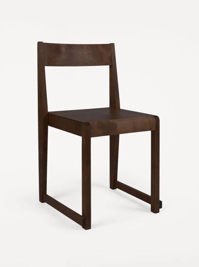 A minimalist dark wooden Chair 01 - Dark Birch with a straight backrest and simple linear design, crafted from Baltic oiled birch. The chair features a solid seat and rectangular legs connected at the bottom. Its Nordic design provides a sleek, modern aesthetic against a plain white background by FRAMA.