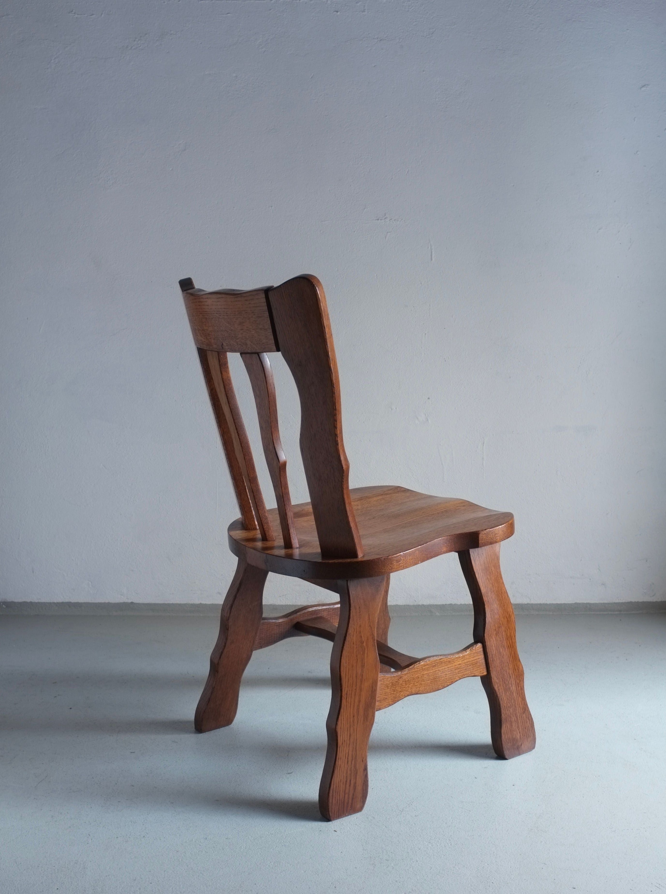 A set of 2 Brutalist Carved Oak Dining Chairs from the 1970s by Veter Vintage, in vintage condition with tall backrests and sturdy legs, positioned against a plain white wall on a light gray floor.