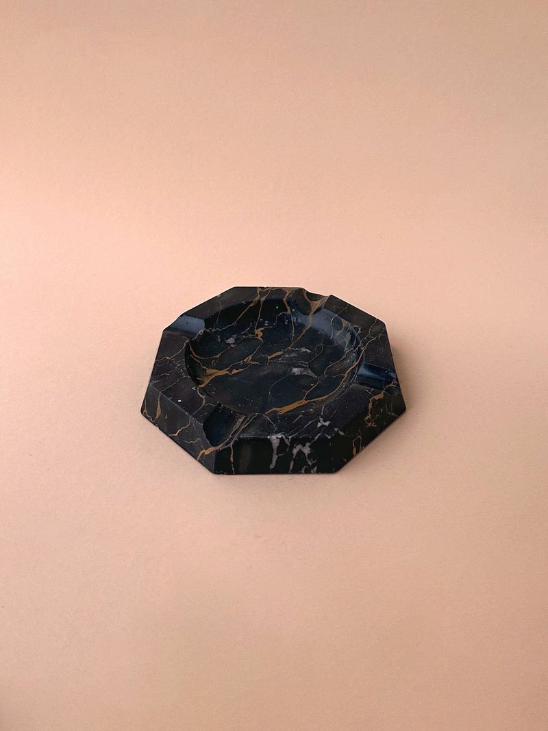 An octagonal 1970s Dodo Vintage black marble ashtray with white and gold veins on a beige background.