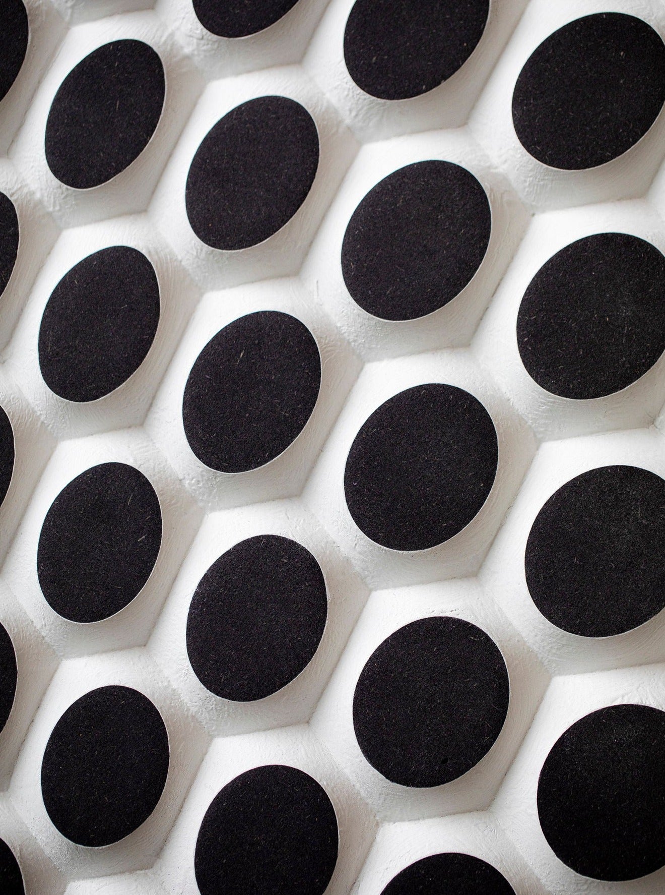 Close-up view of a patterned surface with numerous black circles set in a white foam-like material, creating a contrasting geometric design on a wooden wallpanel of Ommatidium by Studio Arno Hoogland.