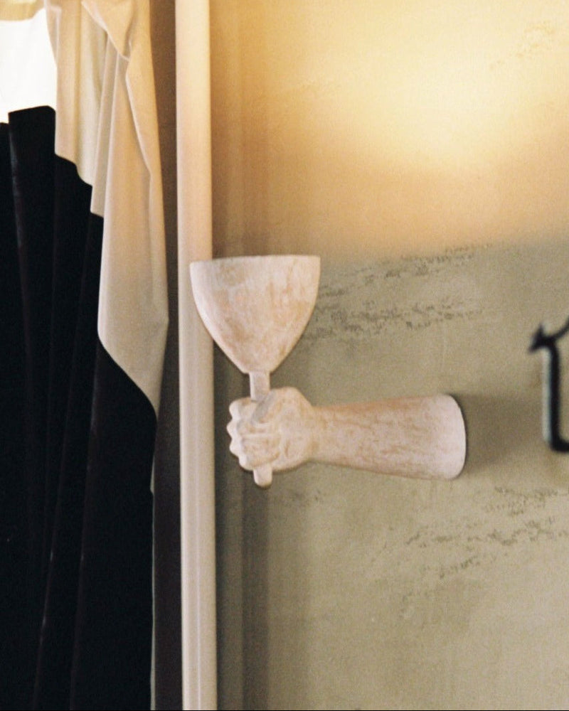 A Dracula Wall Scone Composite mounted on a wall, holding a shallow bowl, with soft lighting reflecting off beige wall surfaces, evoking an elegant and artistic ambiance by Rooms Studio.